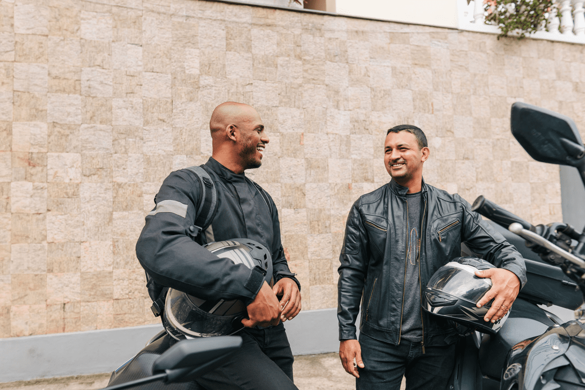 Two motorcyclists smiling with helmets in hand.