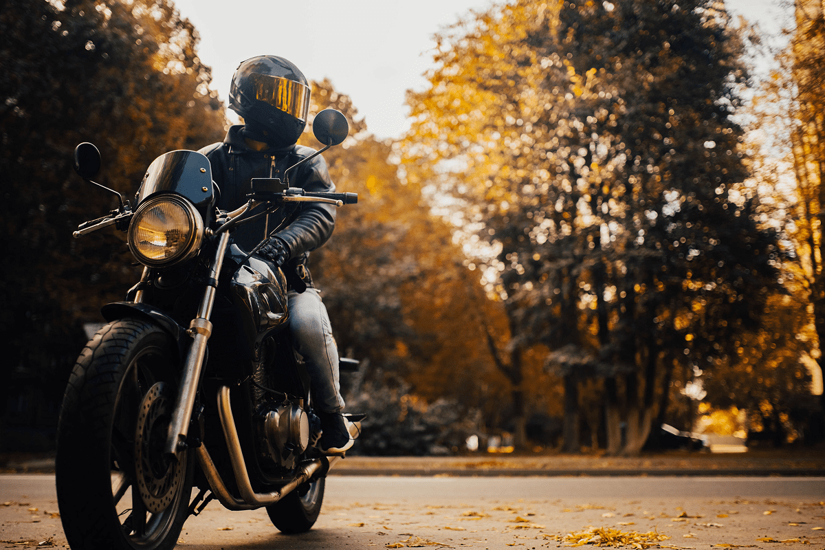 Motorcyclist riding through autumn park scenery.
